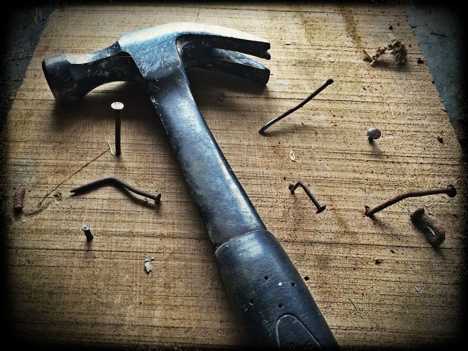 Weathered claw hammer and bent nails on a wooden plank